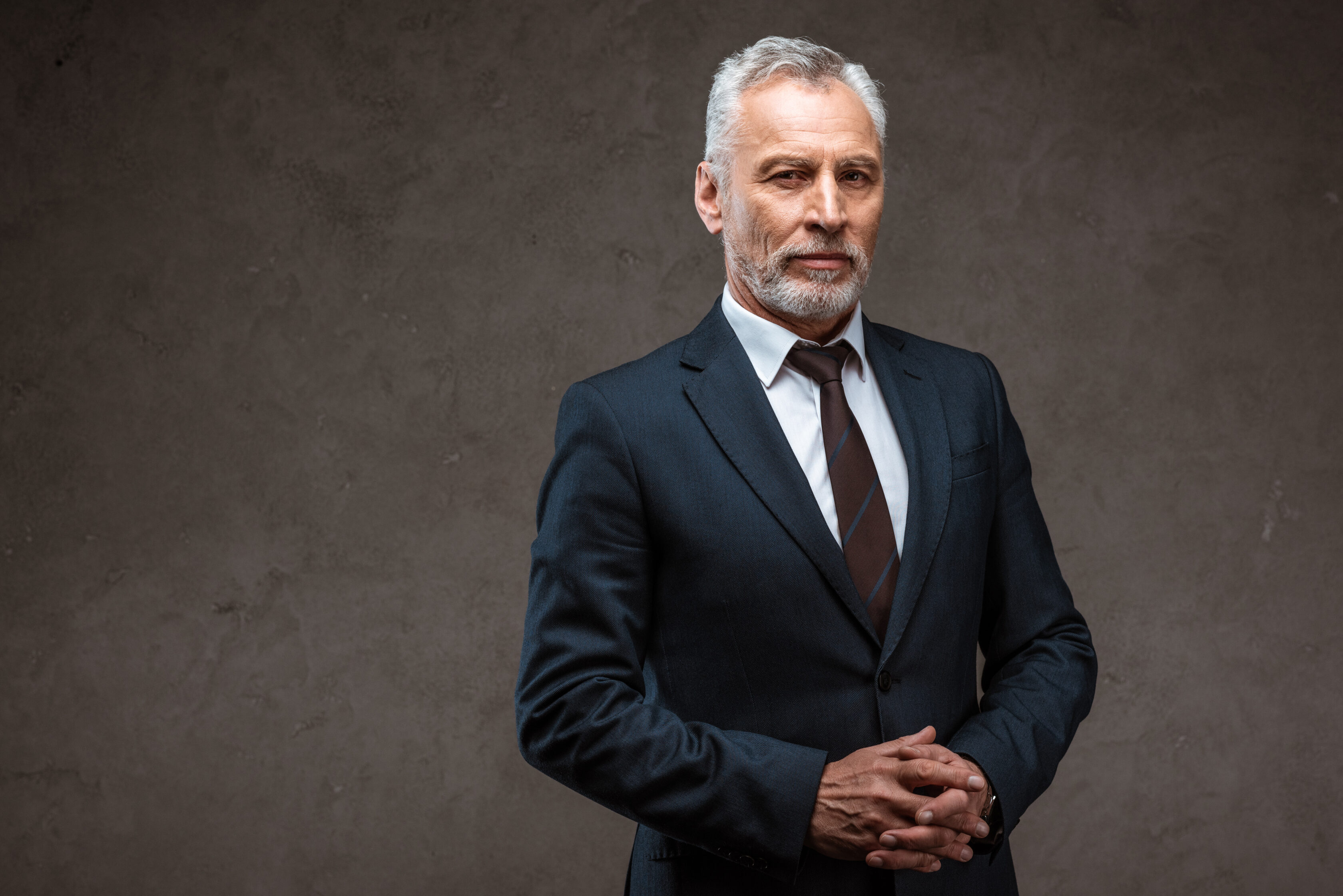 successful businessman in suit standing with clenched hands on grey