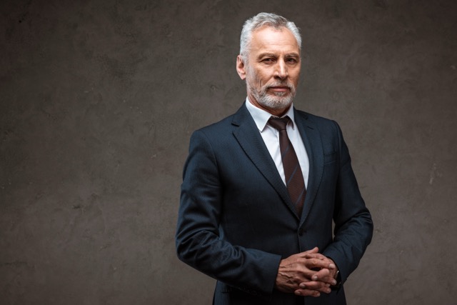 successful businessman in suit standing with clenched hands on grey